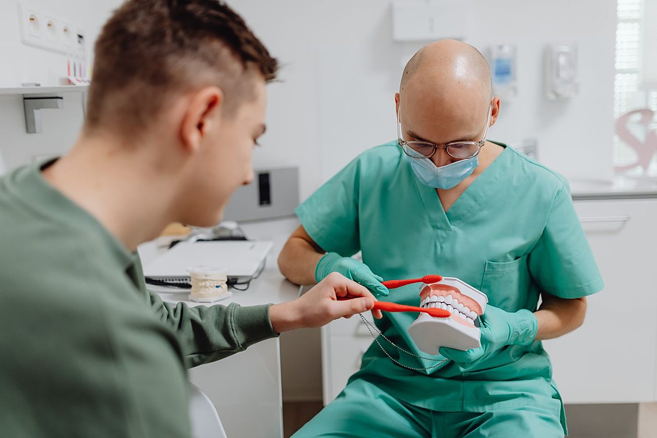Zahnarzt erklärt einem Patienten anhand eines Kiefermodells die richtige Putztechnik